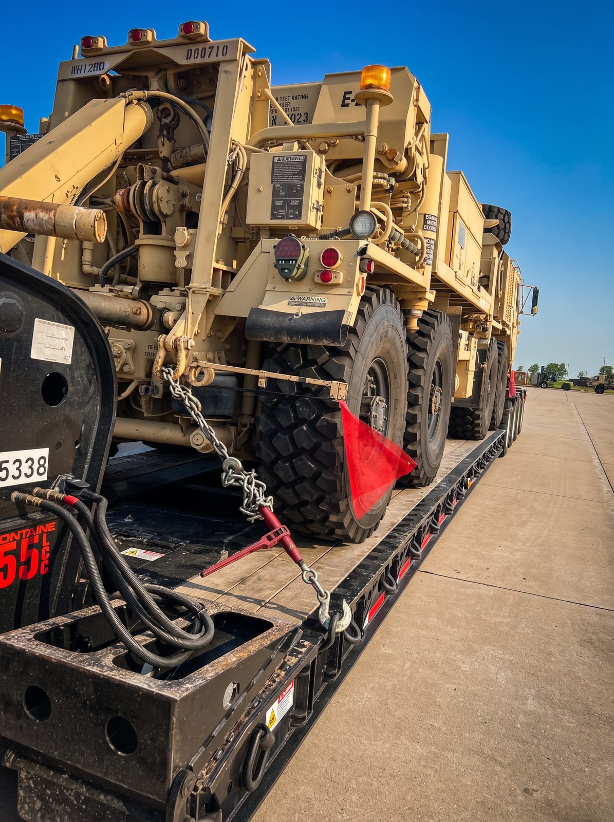 Heavy military recovery vehicle chained and flagged on an extendable lowboy trailer