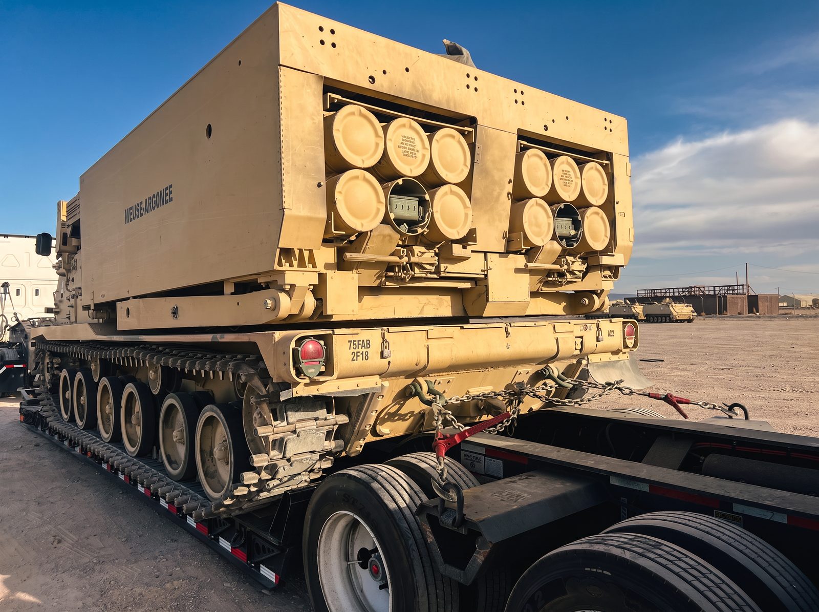 Tracked launcher system chained to a lowboy trailer at a desert equipment yard