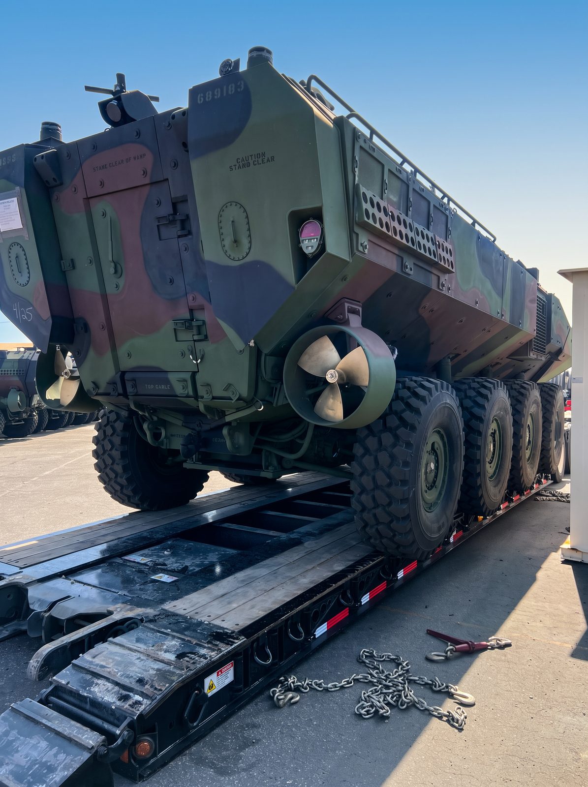 Camouflaged amphibious assault vehicle being driven onto a detachable-gooseneck lowboy ramp