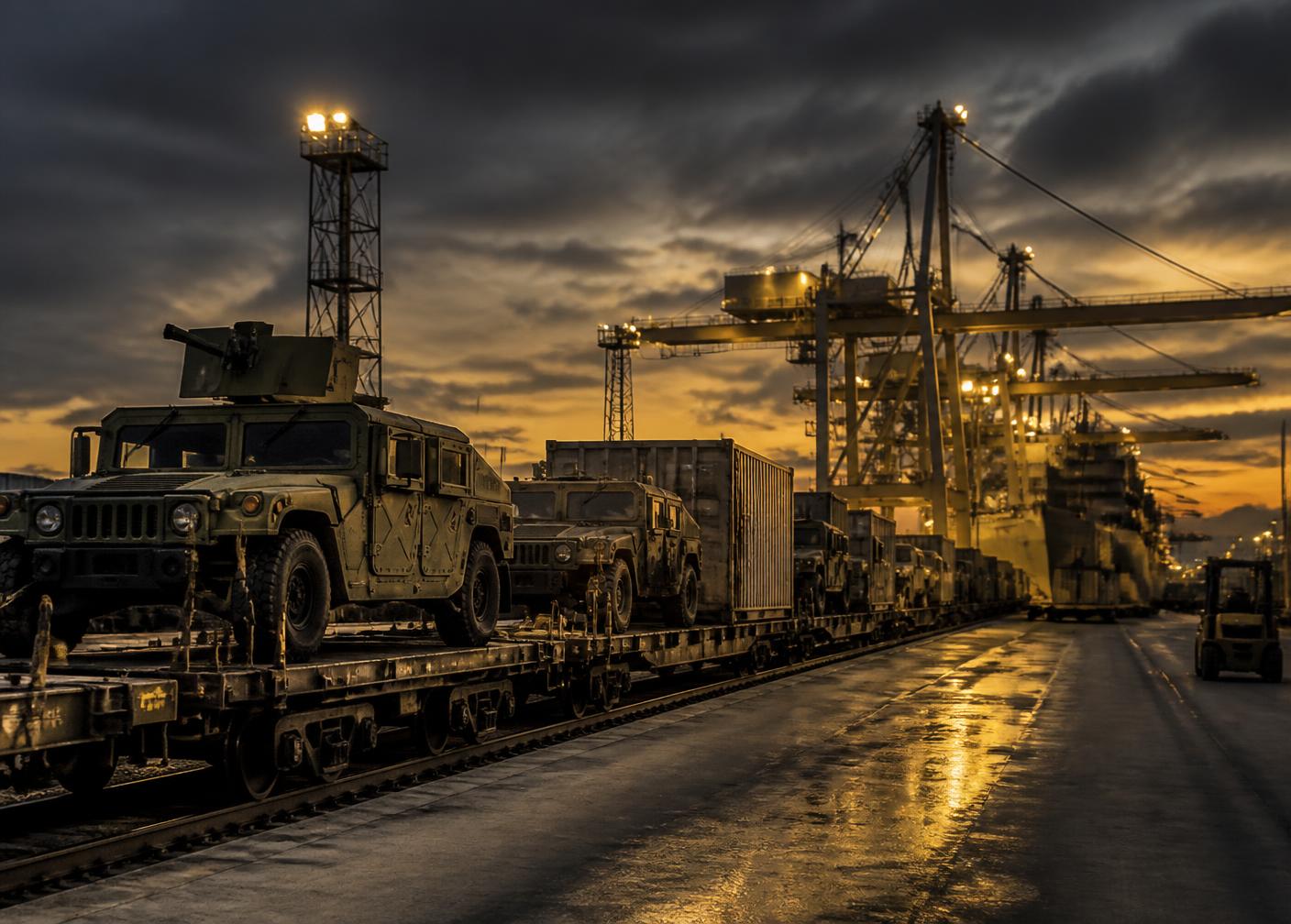 Military cargo and tactical vehicles staged on rail flatcars at a port distribution node