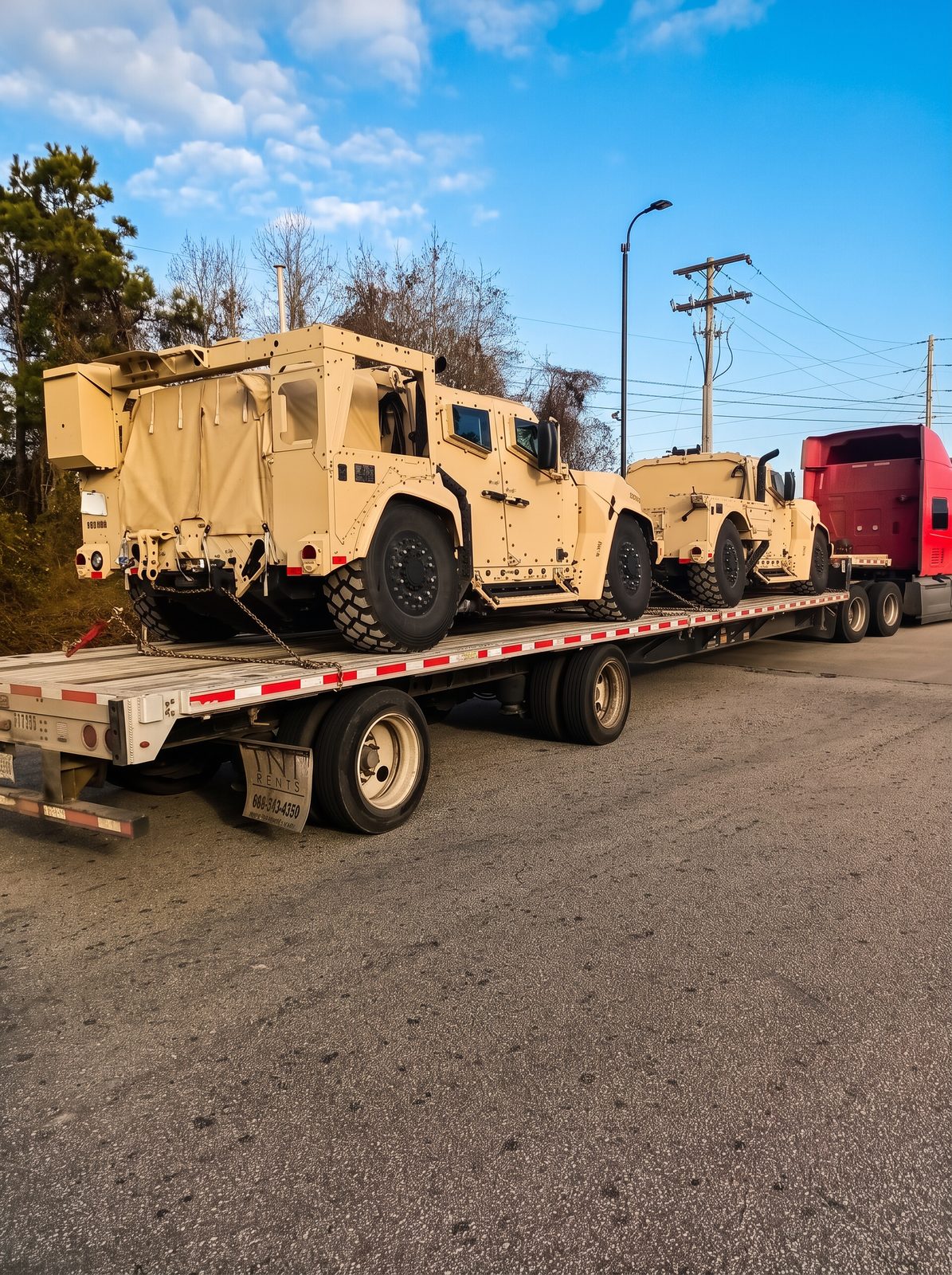 Two tactical armored vehicles chained down on a step-deck flatbed trailer behind a red tractor